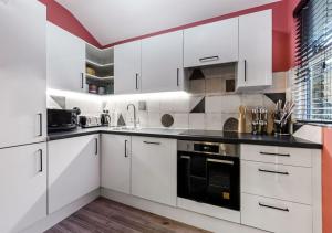 a white kitchen with white cabinets and black appliances at Bright & Colourful House - Best for a Large Groups in London