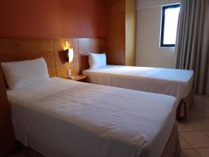 two beds in a hotel room with white sheets at Natal Plaza Suítes- Ponta Negra in Natal