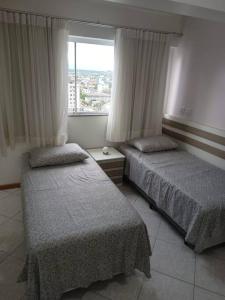 two beds in a room with a window at APARTAMENTO SOLAR DA PRAÇA, Aconchegante e Climatizado in Torres