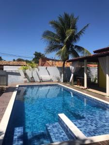 a swimming pool with a palm tree and a house at Village por do sol in Aracaju