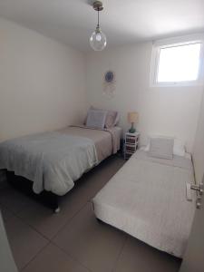 Dos camas en una habitación blanca con ventana. en Departamento Laguna del Mar, en La Serena