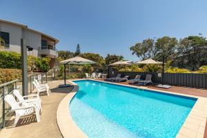 a swimming pool with chairs and umbrellas next to a building at Boom 1 in Blueys Beach