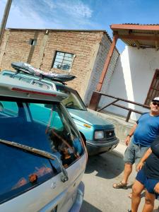 Ein Mann steht neben einem Auto mit einem Surfbrett auf dem Dach in der Unterkunft Casa de mamá María in Malabrigo