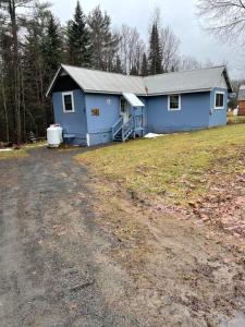 uma casa azul com uma estrada de terra em frente em The Lazy Bear Cabin em Long Lake