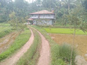 a dirt road in front of a house in a field at Samz estate stay 2BHK in Madikeri