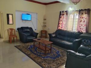 salon z czarnymi skórzanymi meblami i telewizorem w obiekcie Samz estate stay 2BHK w mieście Madikeri