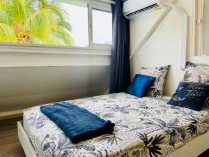 a bed with blue pillows in a room with a window at Lagon, Plage & Détente à La Saline les bains in La Saline les Bains