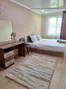 1 dormitorio con cama, escritorio y alfombra en Аппартаменты 2 / х комнатная, en Öskemen