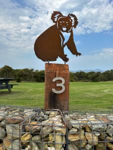 a sign with a bear on top of a wooden post at Tidal Dreaming Seaview Cottages in Yanakie