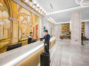 deux hommes debout à un comptoir dans un hall avec bagages dans l'établissement Vienna International Hotel Wudu Gujinli Longnan, à Longnan