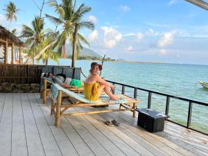 a man sitting on a bench next to the ocean at Namthip Homebeach in Baan Tai