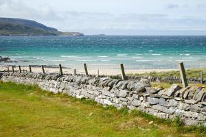 a stone wall next to a beach with the ocean at Balnakeil Cattleman's Bothy in Durness