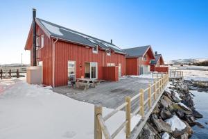 a red building with a wooden deck in the snow at Nappstraumen Seafront Cabin, Lilleeid 68 in Gravdal