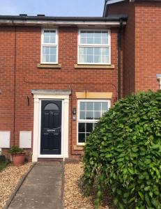 a brick house with a black door and a bush at Homely property close to Princess Royal hospital and Apley Wood in Wellington