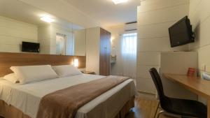 um quarto com uma cama, uma secretária e uma televisão em Hotel Glória Blumenau em Blumenau