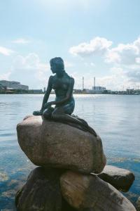 a statue of a mermaid sitting on a rock in the water at Stylish 3-BR Flats in CPH City in Copenhagen