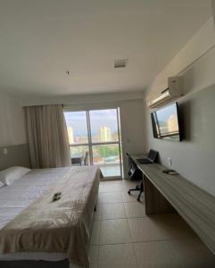 a hotel room with a bed and a desk and a window at Macaé Ramada Flat RJ in Macaé