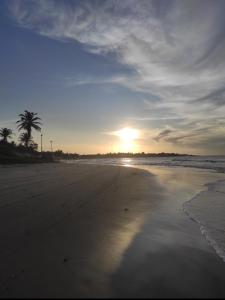 a sunset on a beach with a palm tree at Bangalô pontal beach house in Fortim