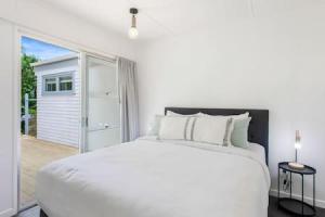 een witte slaapkamer met een bed en een glazen schuifdeur bij Cockle Bay Getaway is close to beach in Auckland