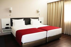 um quarto com uma cama grande com lençóis brancos e vermelhos em Urban Hotel Amadeos em Matosinhos
