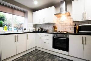 a kitchen with white cabinets and a black oven at Brattan House Oxton Wirral 5 bedroom 3 bathroom with on-street parking ideal for vans by Rework Accommodation in Birkenhead