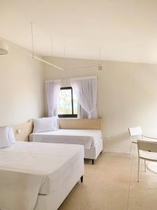 a white bedroom with two beds and a window at Liiv Hub - Natal PontaNegra in Natal
