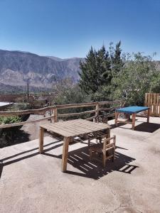una mesa de picnic de madera y un banco con montañas en el fondo en El Cerrito en Maimará