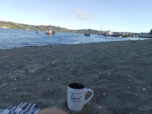 uma chávena de café sentada numa praia junto à água em Hostal Sandrita em Castro
