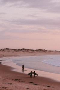 Guesthouse Beach Break في بينيش: مجموعة من الناس تقف على شاطئ مع ألواح ركوب الأمواج