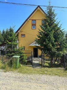 una casa amarilla con una valla y un árbol en Casa valea gilortului, en Ranca