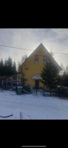 Une grande maison jaune avec de la neige devant elle dans l'établissement Casa valea gilortului, à Rânca
