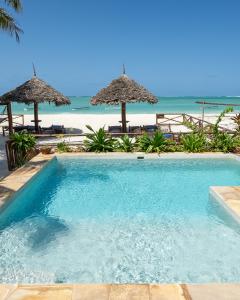a swimming pool next to a beach with umbrellas at Villa Thamani Zanzibar in Pwani Mchangani