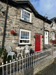 a stone house with a red door and a table and chairs at Maytree Cottage. Compact home in Mid Wales. in Llanrhaeadr-ym-Mochnant