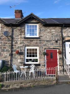 a stone house with a red door and a white fence at Maytree Cottage. Compact home in Mid Wales. in Llanrhaeadr-ym-Mochnant