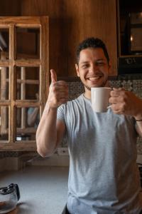 un homme tenant une tasse de café et donnant un pouce dans l'établissement Privada y comoda cabaña, Casa Margarita, Villavieja, à Villavieja