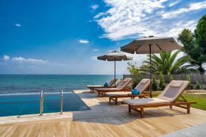 a pool with chairs and umbrellas next to the ocean at Violet Beach Front Private Villa in Laganas