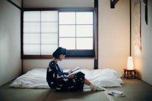 une femme assise sur un lit en train de lire un livre dans l'établissement Casa OGUMO - Vacation STAY 34543v, à Kyoto