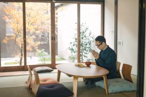un homme assis à une table et regardant son téléphone portable dans l'établissement Casa OGUMO - Vacation STAY 34543v, à Kyoto