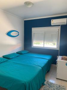 a blue bedroom with two beds and a window at Residencial Ametista - 250 metros do mar in Florianópolis