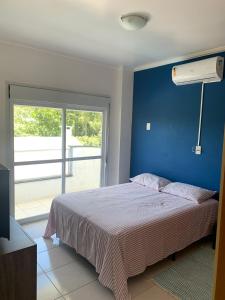 1 dormitorio con 1 cama con pared azul y ventana en Residencial Ametista - 250 metros do mar, en Florianópolis