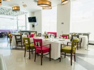 HS HOTSSON Hotel Queretaro في كيريتارو: غرفة طعام مع طاولات بيضاء وكراسي ملونة