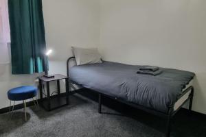 a bed in a room with a lamp and a stool at Sunrise at Clippie, 3 Rooms, 4 Beds, Recently Renovated, Free WiFi, Free Street Parking, Ground Floor, Fully Equipped, Favourite for Groups, Contractors and Trades, Short and Long Stays Welcome at Sunrise Short Lets Dundee in Dundee