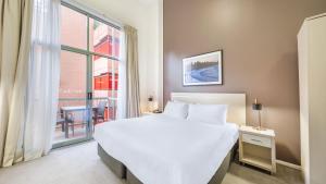 Un dormitorio con una gran cama blanca y una ventana en Oaks Sydney Goldsbrough Suites en Sídney