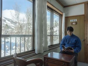 um homem a ler um livro numa sala com uma janela em 古民家ホテル 結 YUWAI em Hakuba