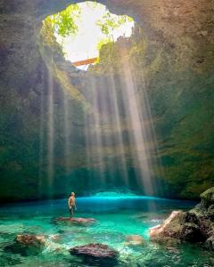 a man standing on a rock in a river with a waterfall at Glowing Mountain view tree house in Loanengo