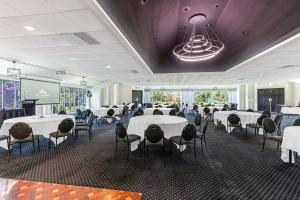 un salón de banquetes con mesas y sillas blancas y una pantalla de proyección en All Seasons Resort Hotel Bendigo, en Bendigo