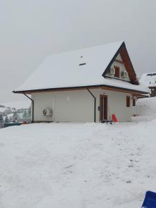 een huis met een met sneeuw bedekt dak in de sneeuw bij Domki na kocim zamku in Grywałd