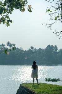 a woman standing in front of a lake at Cranganor History Café & Riverside Château in Parūr