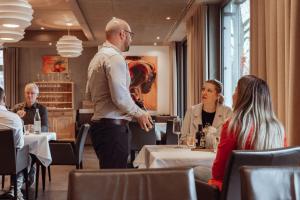 un hombre de pie en un restaurante con gente sentada en las mesas en Encanto Hotel Restaurant, en Balingen