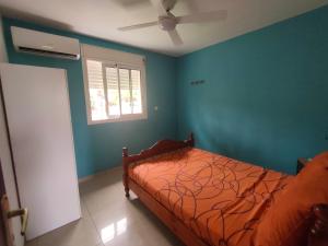 - une chambre avec un lit aux murs bleus et une fenêtre dans l'établissement Petite maison à 12mn du bassin de Manapany, à Saint-Joseph